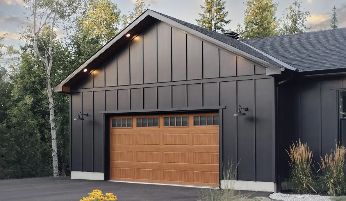 Wood-grain steel plank garage door on a dark modern barn-style garage.