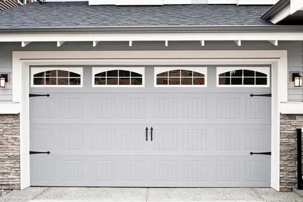 White sectional garage door with small upper windows on a stone-front home.